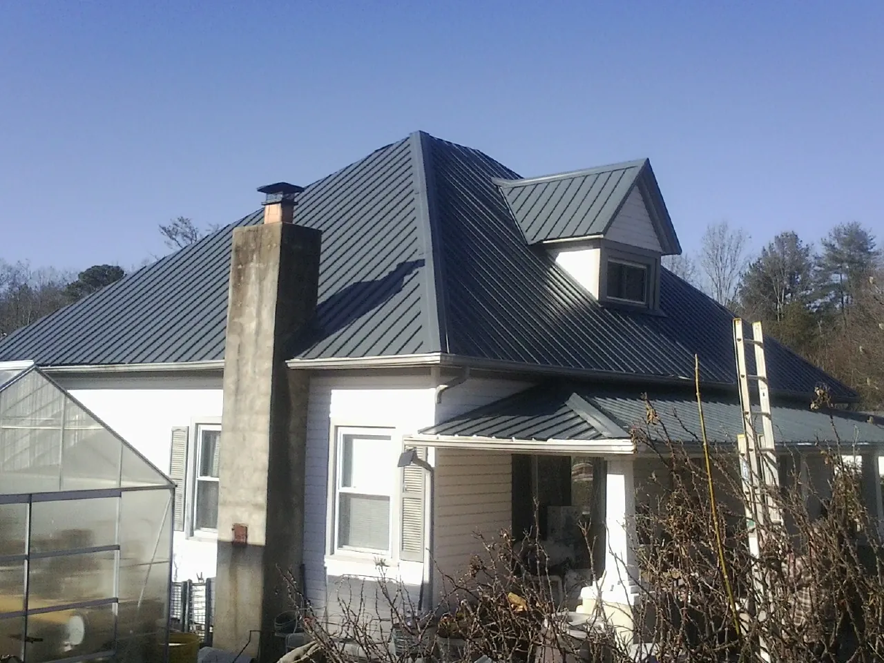 Dark blue standing seam metal roof on a white farmhouse with dormer — Slate & Tile Roof Repair by Roofing Brothers in Kewanee