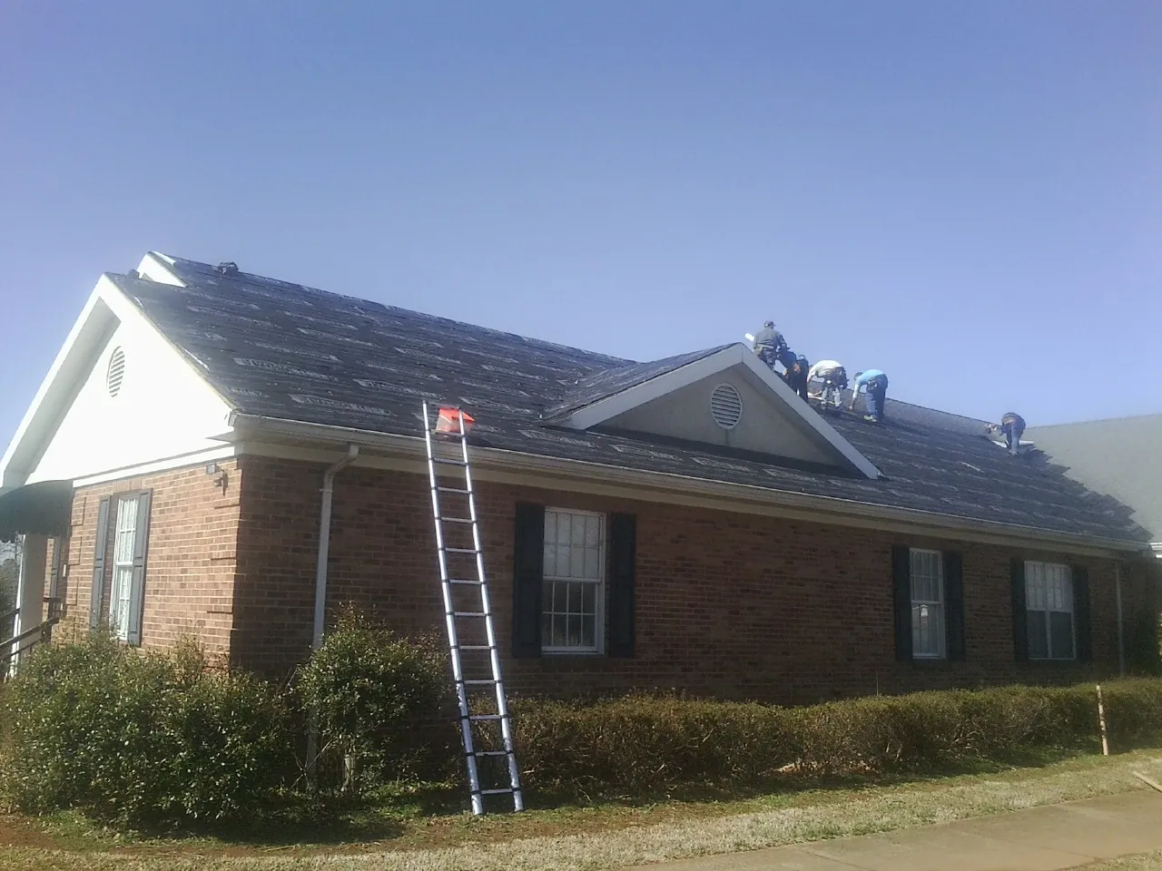 Crew tearing shingles off a brick ranch roof with a ladder set — Metal Roof Repair work by our crew in Kewanee