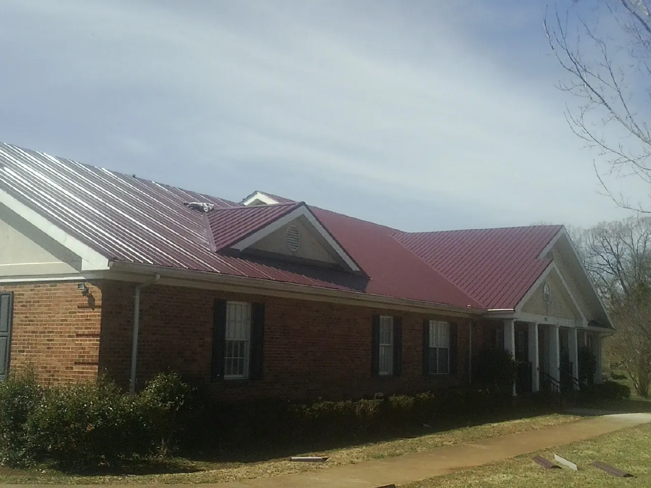 Red metal roof with gabled entries on a long brick building, from a Hail Damage Roof Repair job in Kewanee