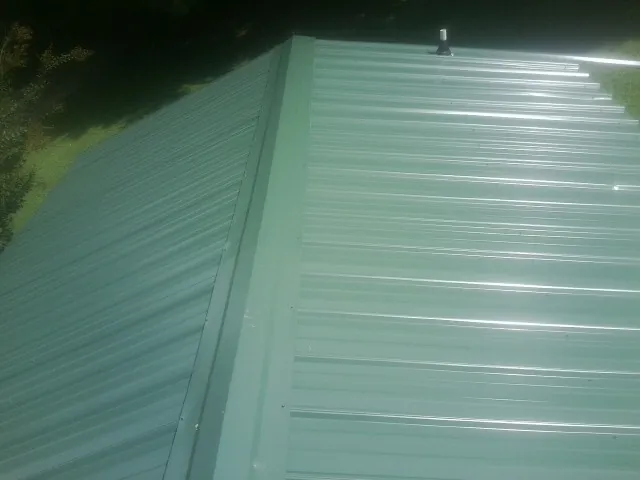 New green metal panels meeting at the ridge of a roof — Flat Roof Repair work by our crew in Kewanee