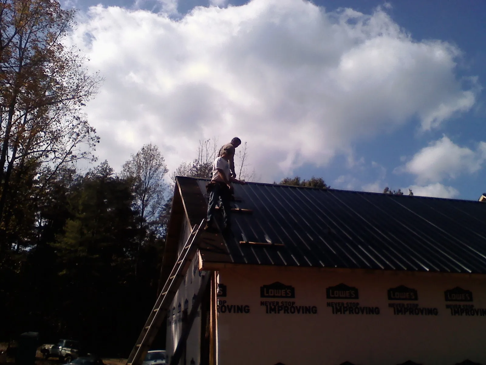 Roofer fastening dark metal panels high against a cloudy sky, from a Roof Inspection job in Kewanee