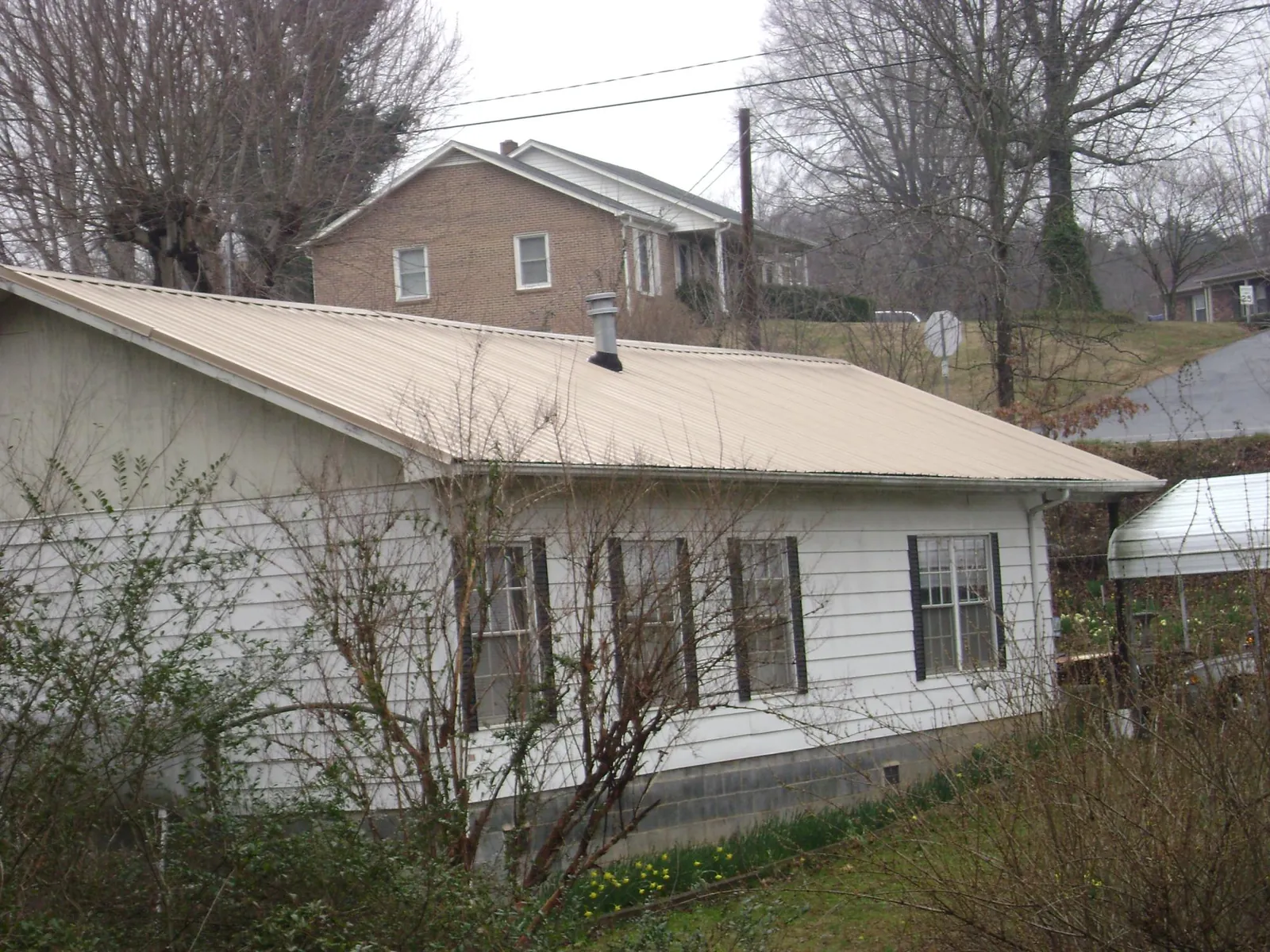 Tan metal roof on a white sided house set into a hillside — Commercial Roofing by Roofing Brothers in Kewanee
